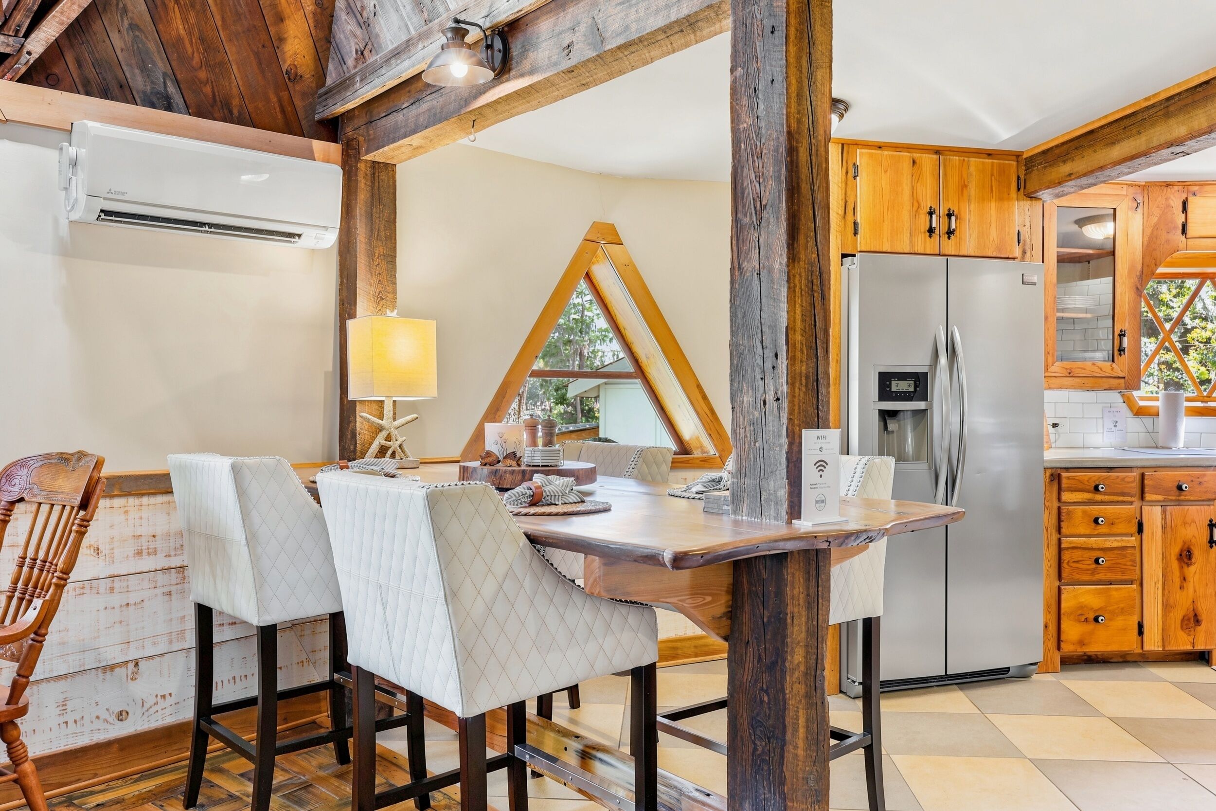 A rustic kitchen with wooden cabinets, a stainless steel refrigerator, and a dining area with a wooden table and chairs.