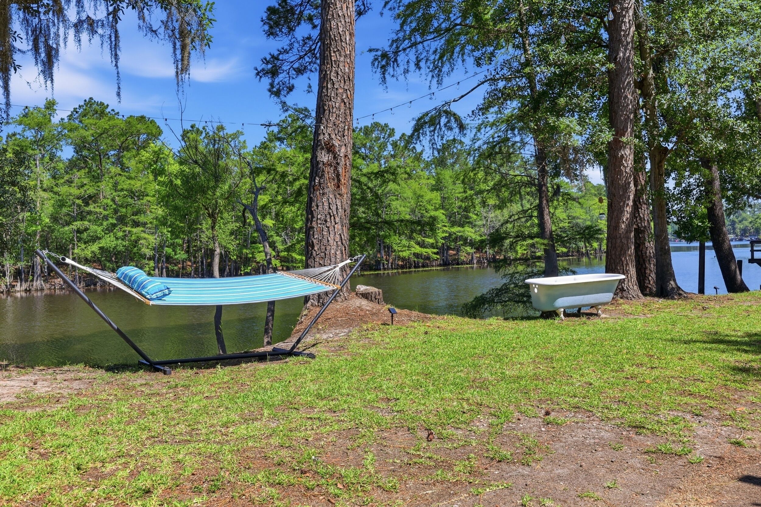 A hammock and a bathtub near a lake surrounded by trees.