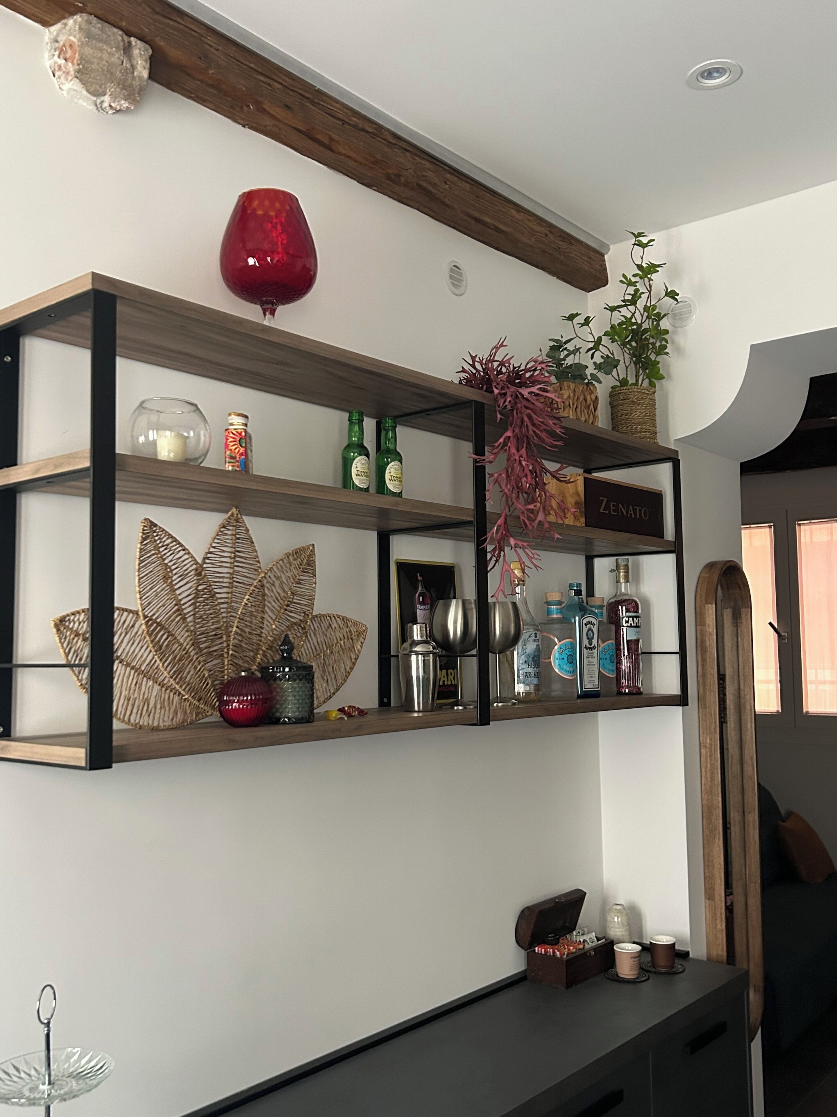 Ein Regal mit Dekoration, darunter eine rote Vase, Flaschen und ein Schild mit der Aufschrift 'ZENATO'.