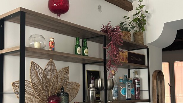Uma prateleira com objetos decorativos, incluindo um vaso vermelho, garrafas e uma placa com a inscrição 'ZENATO'.