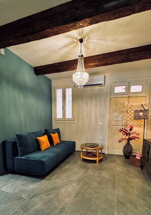 Ein Wohnzimmer mit einem dunkelblauen Sofa, einem Holztisch, einer Kristallleuchtre und einem großen Fenster.