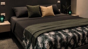 Quarto moderno com cama, mesas de cabeceira, um quadro emoldurado e um vaso com plantas.