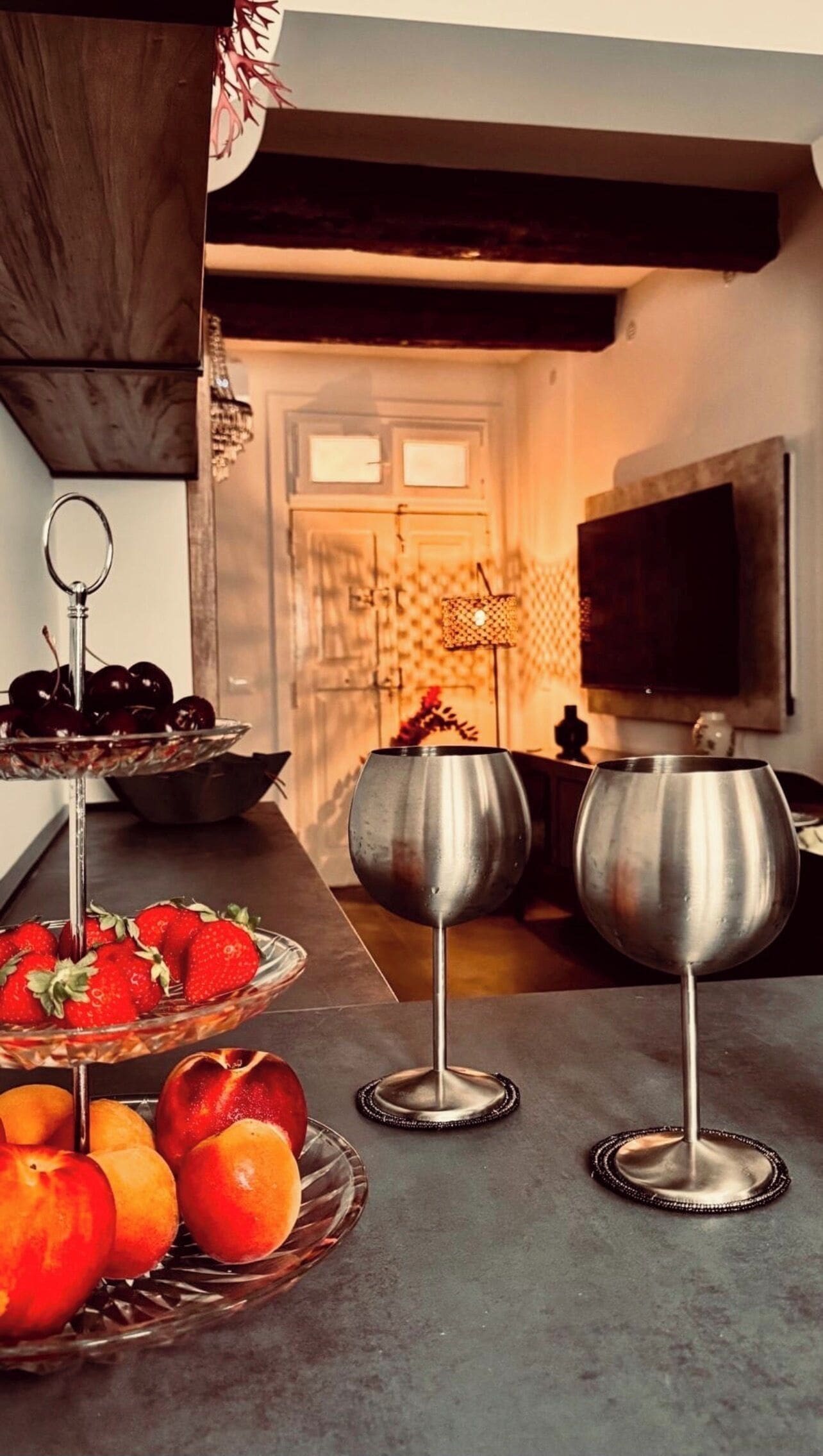 A kitchen counter with fruit bowls and two metal wine glasses.