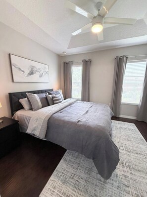 A bedroom with a bed, a ceiling fan, a nightstand, a rug, and a window with curtains. - 3BD 3BR Stylish Disney Retreat 15 Mins to Disney (Kissimmee)