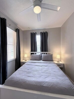 Ein Schlafzimmer mit einem Bett, zwei Nachttischen mit Lampen, einem Deckenventilator und einem Fenster mit Vorhängen.