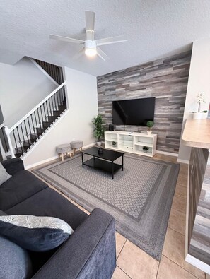 A living room with a sofa, coffee table, TV, and a staircase. - 3BD 3BR Stylish Disney Retreat 15 Mins to Disney (Kissimmee)