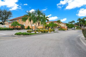 A gated parking area with a road leading to a building with a red-tiled roof. - 3BD 3BR Stylish Disney Retreat 15 Mins to Disney (Kissimmee)