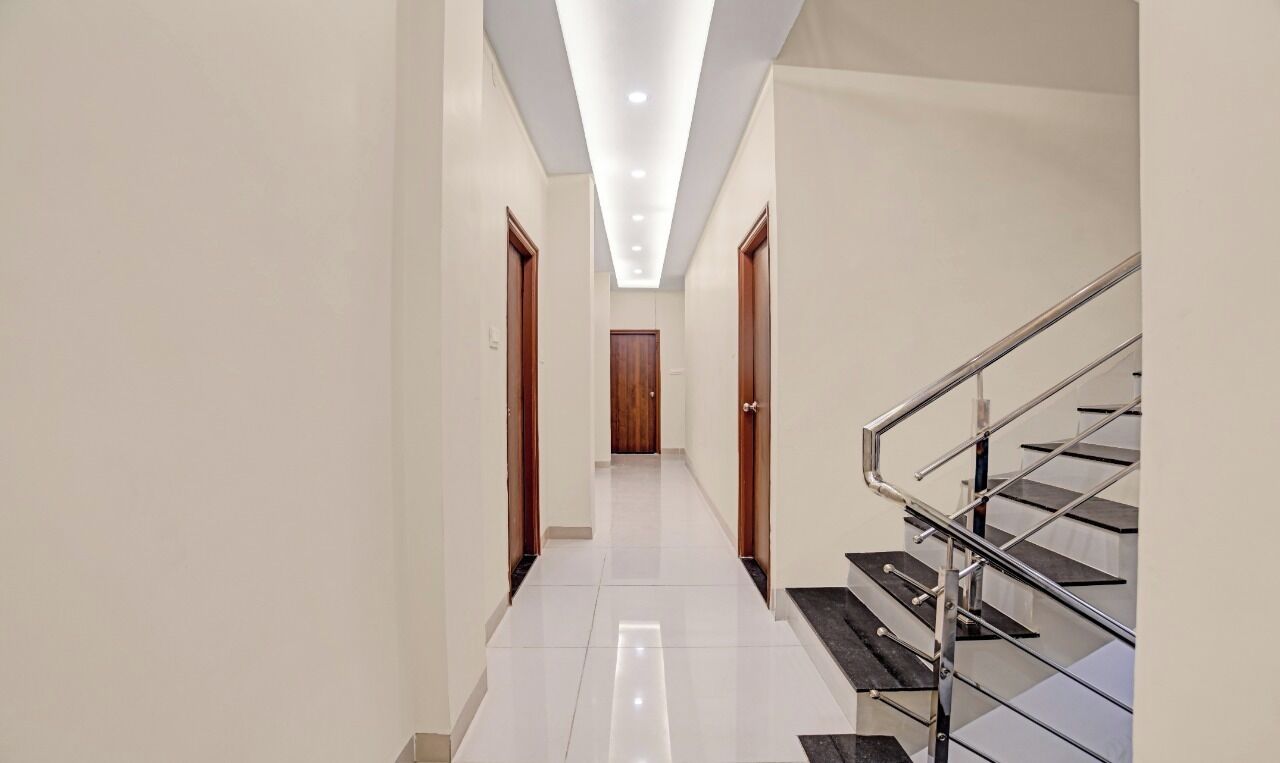 A modern hallway with a staircase, white tiled flooring, and recessed ceiling lighting.