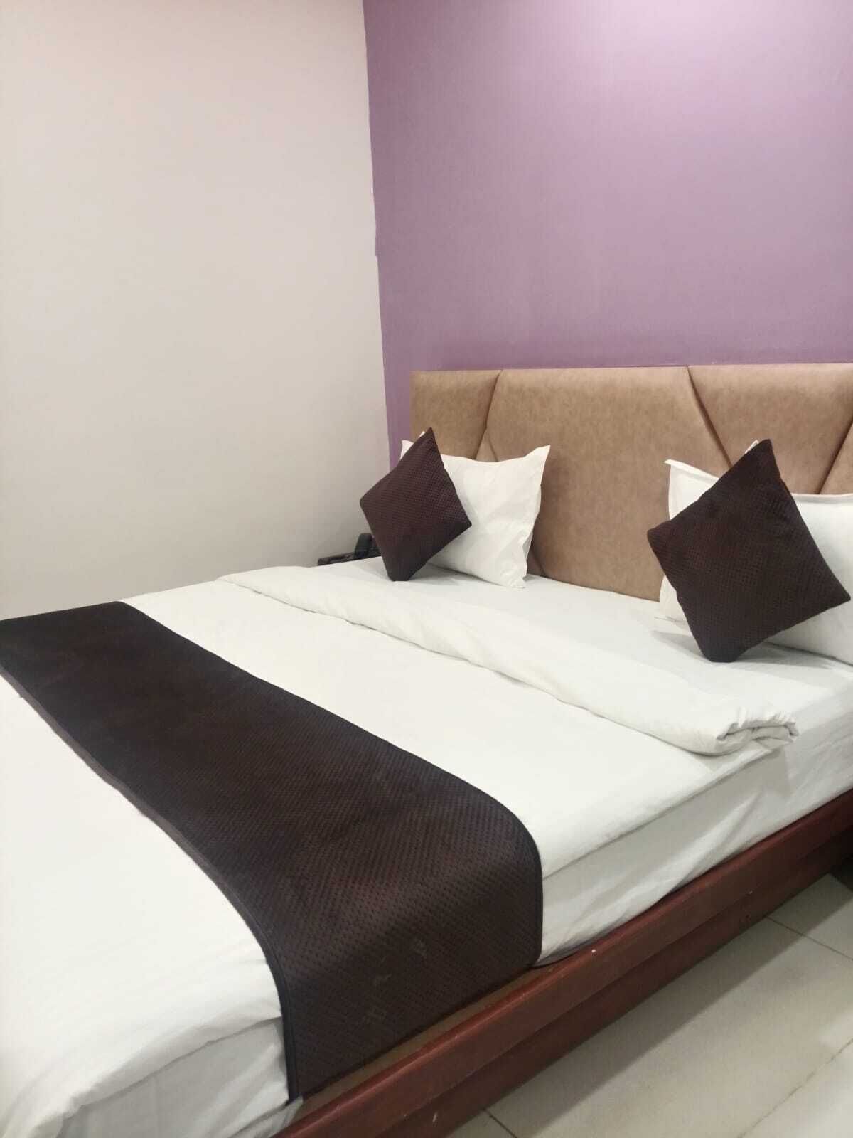Una cama con cabecera, ropa de cama blanca y dos almohadas oscuras.