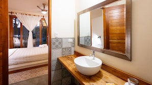 Un dormitorio con cama, mesita de noche, espejo y ventana con cortinas.
