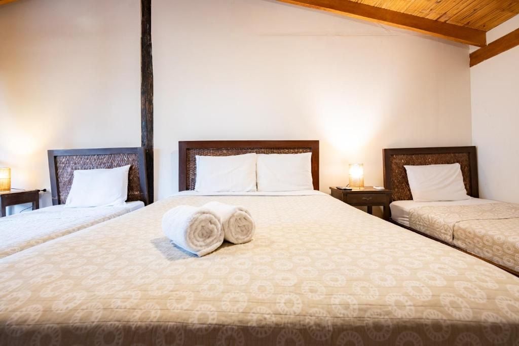 A hotel room with two beds, each with a headboard, and a large bed in the center. There are two bedside tables with lamps.