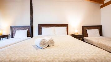 A hotel room with two beds, each with a headboard, and a large bed in the center. There are two bedside tables with lamps.