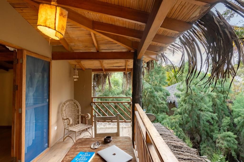 Um deck de madeira com telhado de palha, um laptop e uma cadeira.