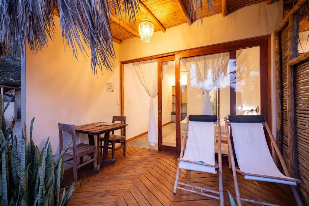 A wooden deck with a table and chairs, a pair of sun loungers, and a glass door leading to an interior space.