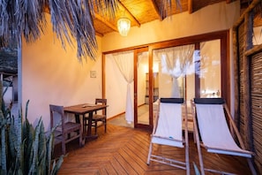 A wooden deck with a table and chairs, a pair of sun loungers, and a glass door leading to an interior space.