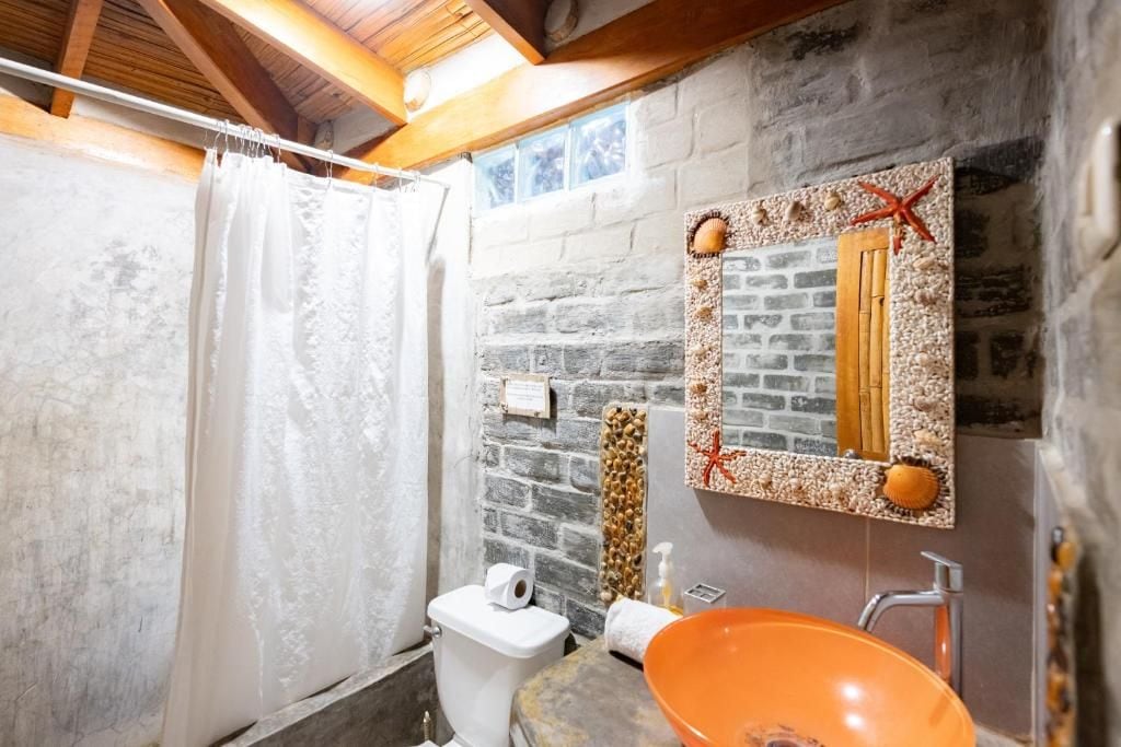 Et badeværelse med badeforhæng, toilet, håndvask med orange skål og et dekorativt spejl med en stjernefisk-pynt.