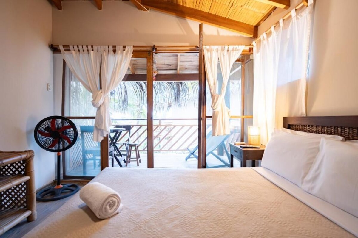Una habitación de hotel con una cama, un ventilador, una mesa y vistas al exterior.