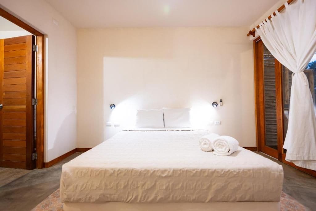 A hotel room with a large bed, a wooden door, and a window with curtains.