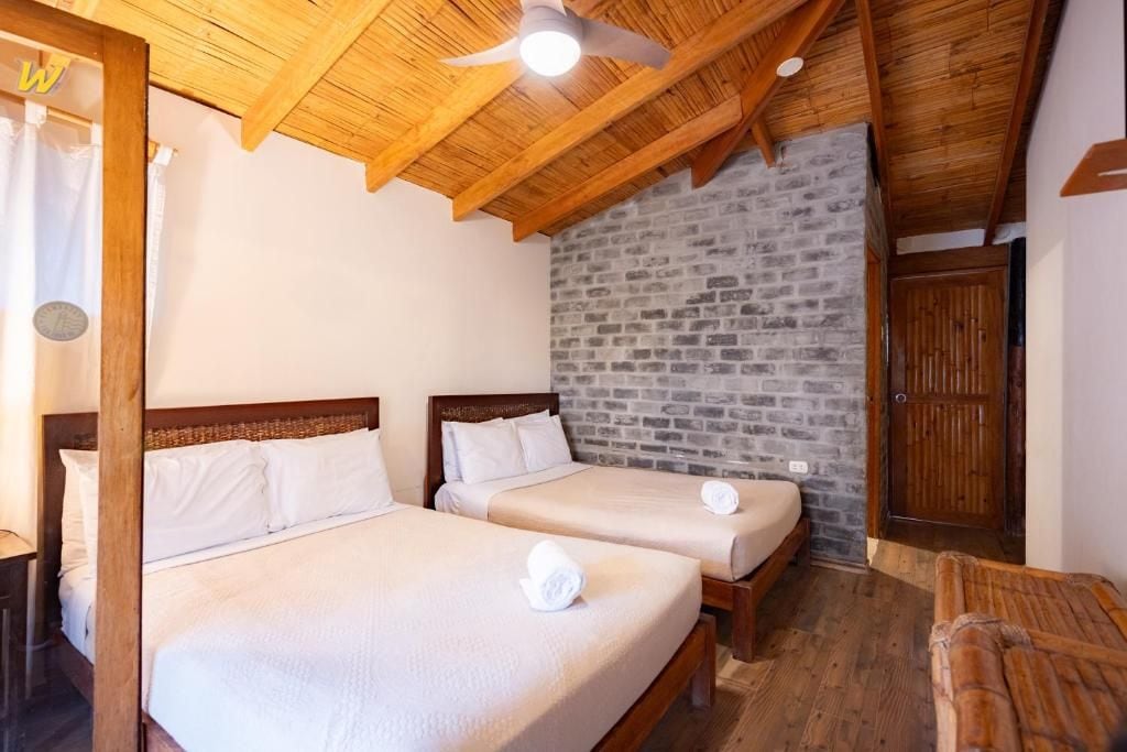 A room with two beds, wooden beams, a stone wall, and a wooden door.