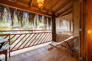 A wooden deck with a wooden bench, a hammock, and a view of greenery.