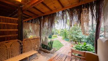 Ein Sitzbereich im Freien mit gewebten Stühlen und einem Holztisch, umgeben von einem Garten mit einem Weg und verschiedenen Pflanzen.