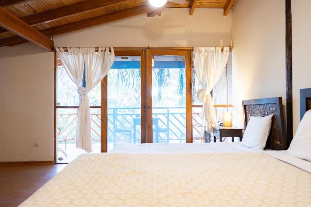 Una habitación de hotel con cama, cortinas, mesita de noche y vistas al exterior.