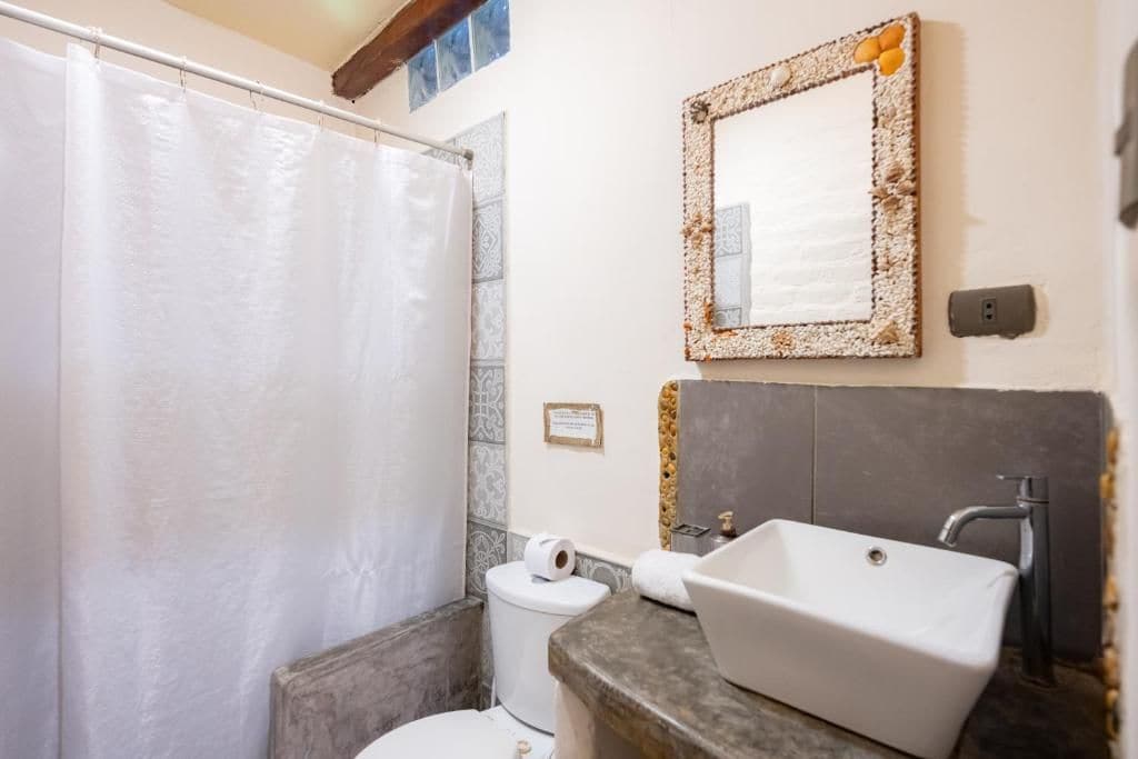 A bathroom with a shower curtain, a sink with a mirror, and a toilet.