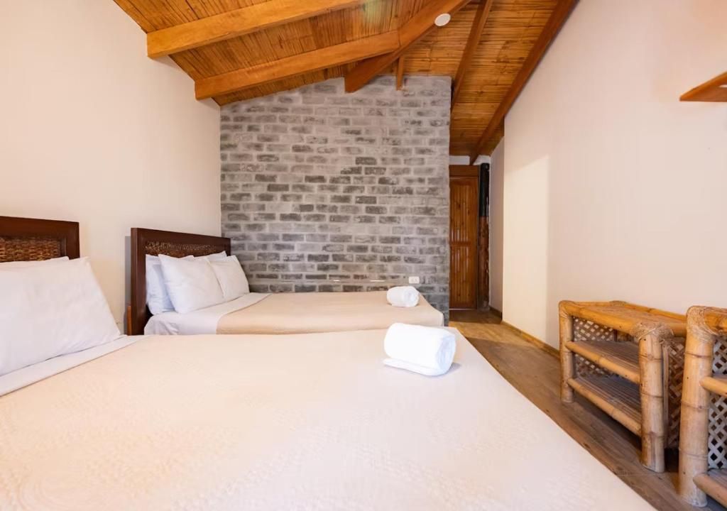 Une chambre avec deux lits, un mur en pierre, des poutres apparentes en bois au plafond et un banc en bois.
