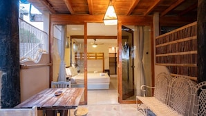 Un interior de madera con una mesa, sillas y un banco. Se ve una cama y un baño a través de una puerta de cristal.