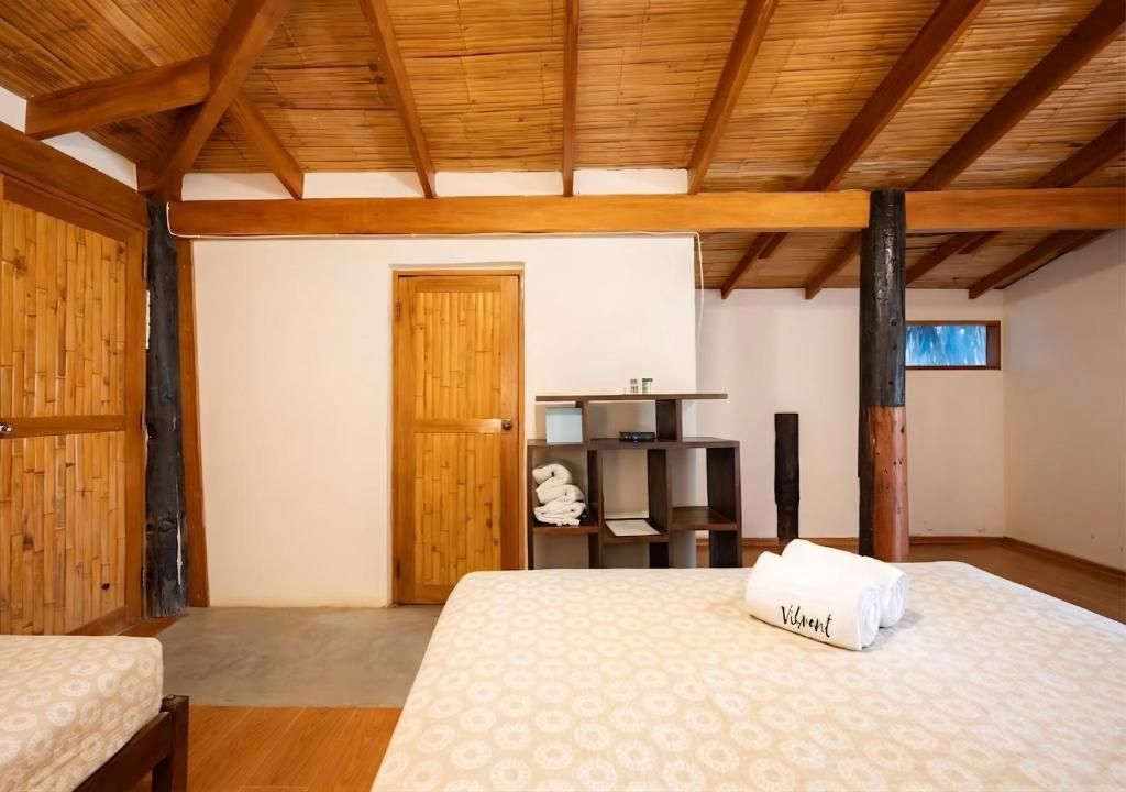 A bedroom with a wooden ceiling, a bed with a patterned bedspread, a wooden wardrobe, and a small table with a chair.