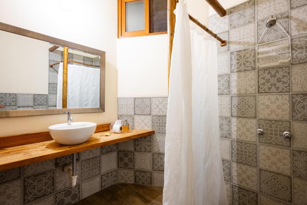 A bathroom with a wooden vanity, a white sink, a mirror, and a shower area with patterned tiles.