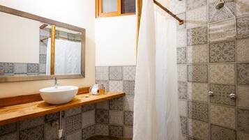 A bathroom with a wooden vanity, a white sink, a mirror, and a shower area with patterned tiles.