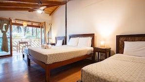 Habitación de hotel con dos camas, piso de madera, ventilador de techo y balcón con vistas.