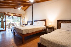 A hotel room with two beds, wooden flooring, a ceiling fan, and a balcony with a view. - Hospedaje La Quebrada - Mancora - Perú  (Máncora)