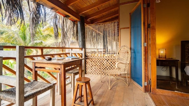 Una terraza de madera con una mesa, sillas y un sillón de mimbre, además de una puerta azul.