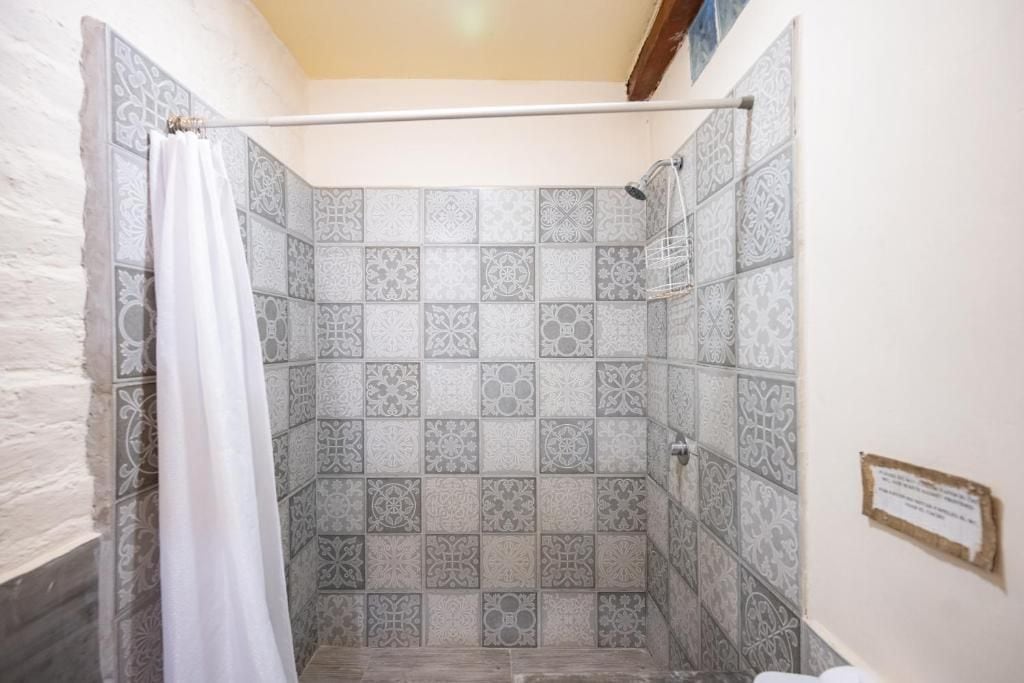 A shower with a white curtain, tiled walls with a geometric pattern, and a wooden beam above.