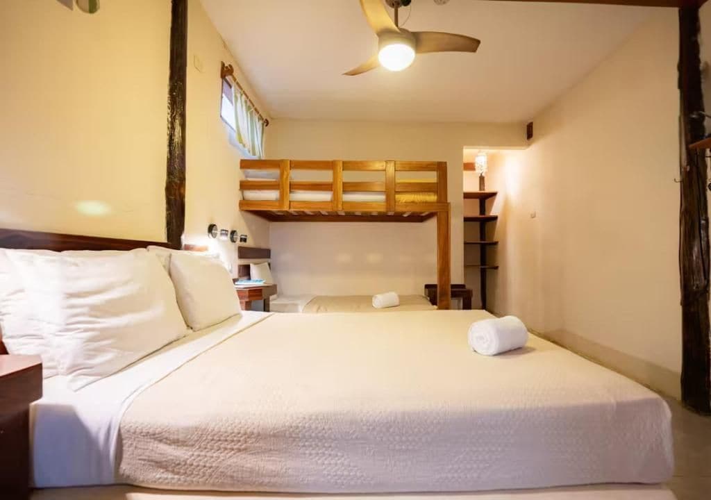 Une chambre d’hôtel avec un lit superposé, une table de chevet, une lampe et un ventilateur de plafond.