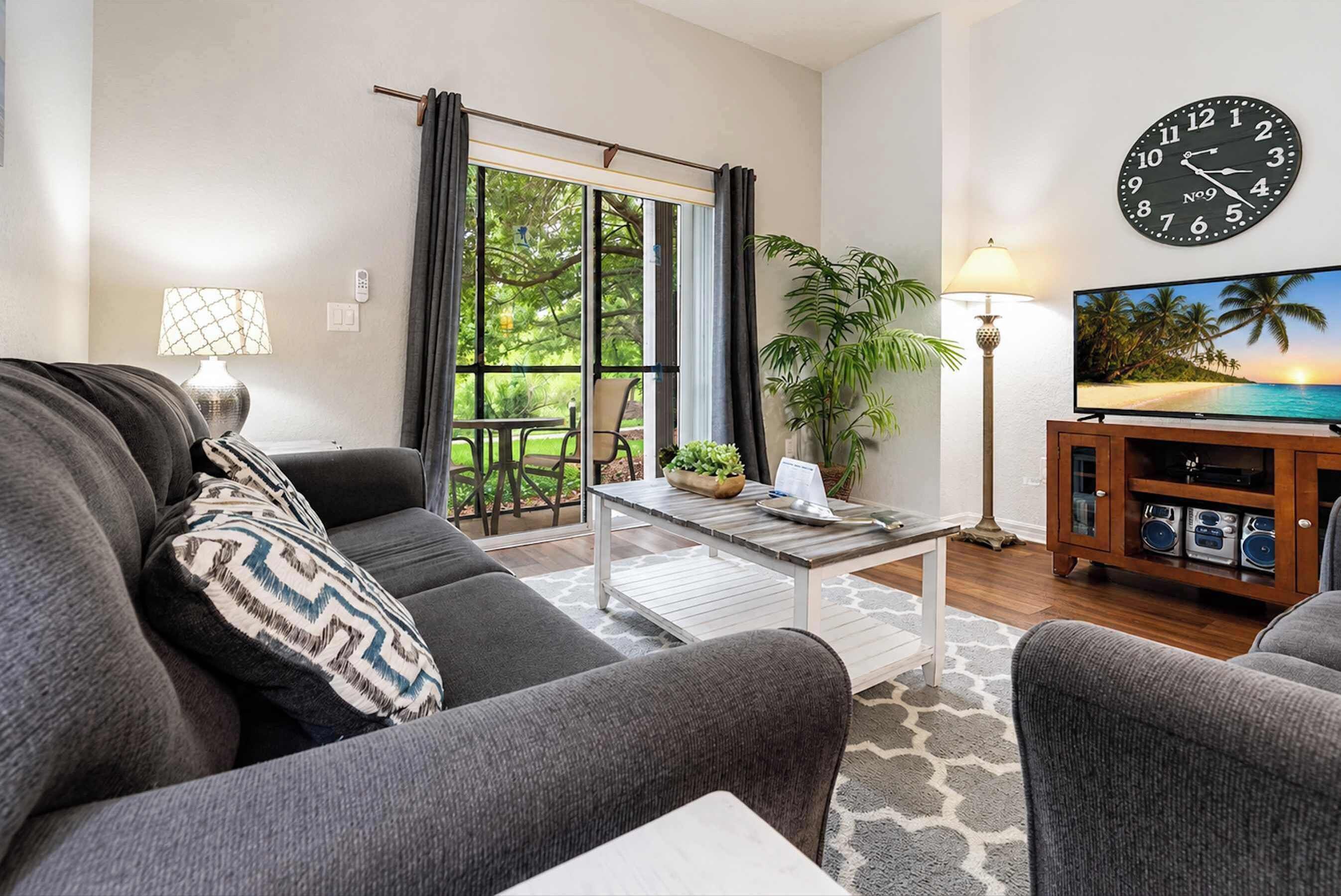 A living room with a sofa, coffee table, TV stand, and a large wall clock.