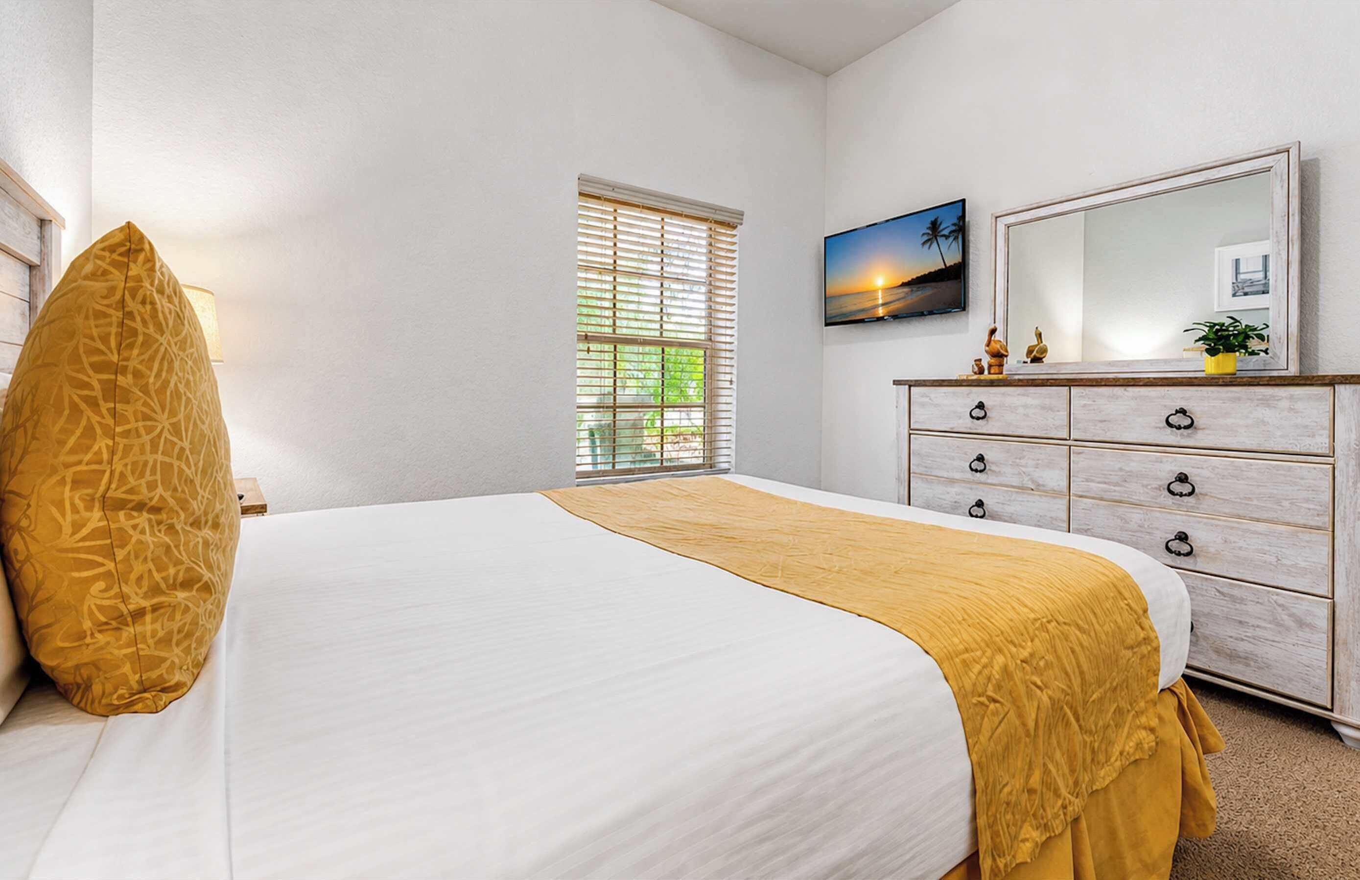 A bedroom with a bed, a dresser, a window with blinds, a painting, and a mirror.