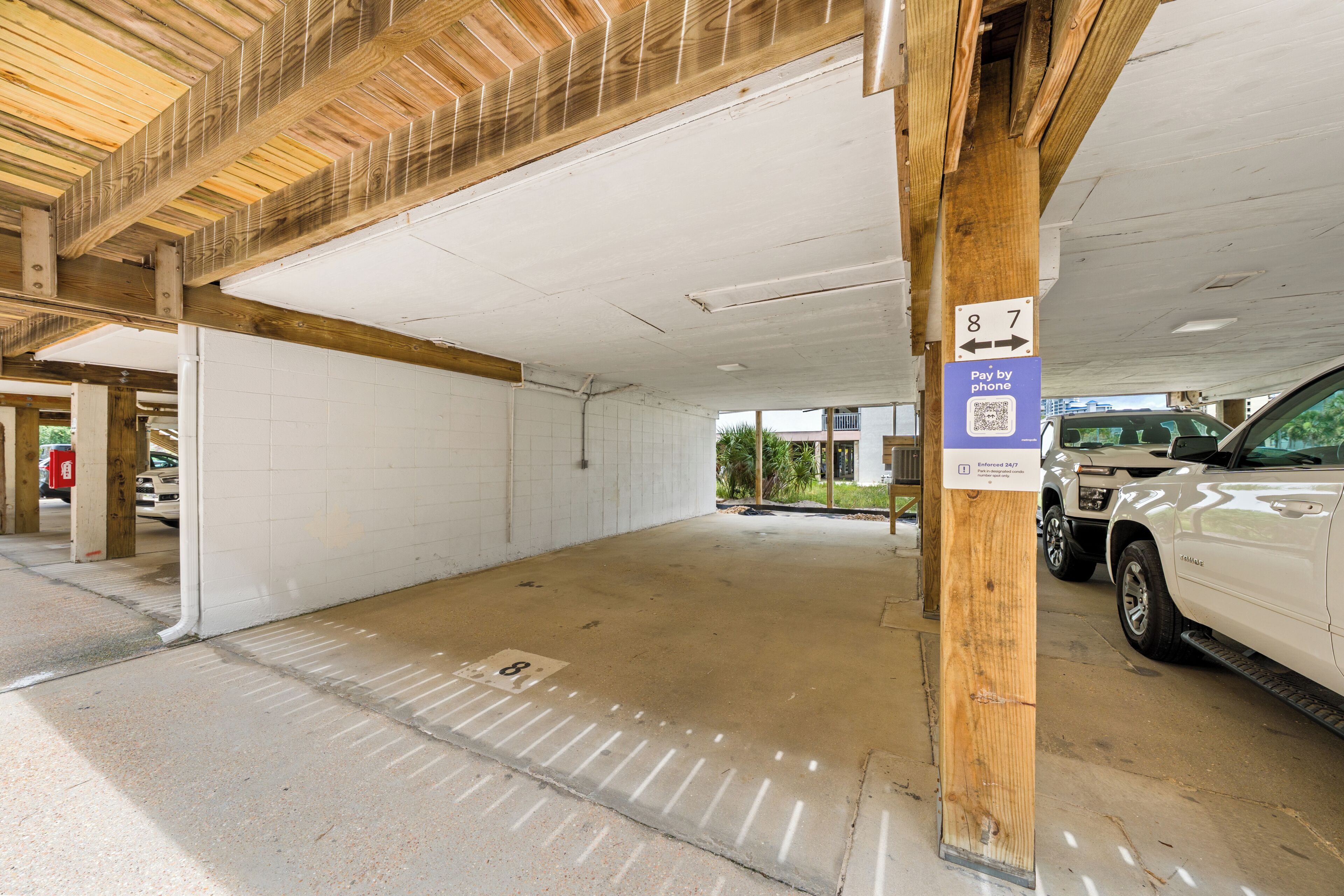 A parking garage with concrete floors, white walls, and a wooden ceiling. There are signs indicating parking spots and payment instructions.