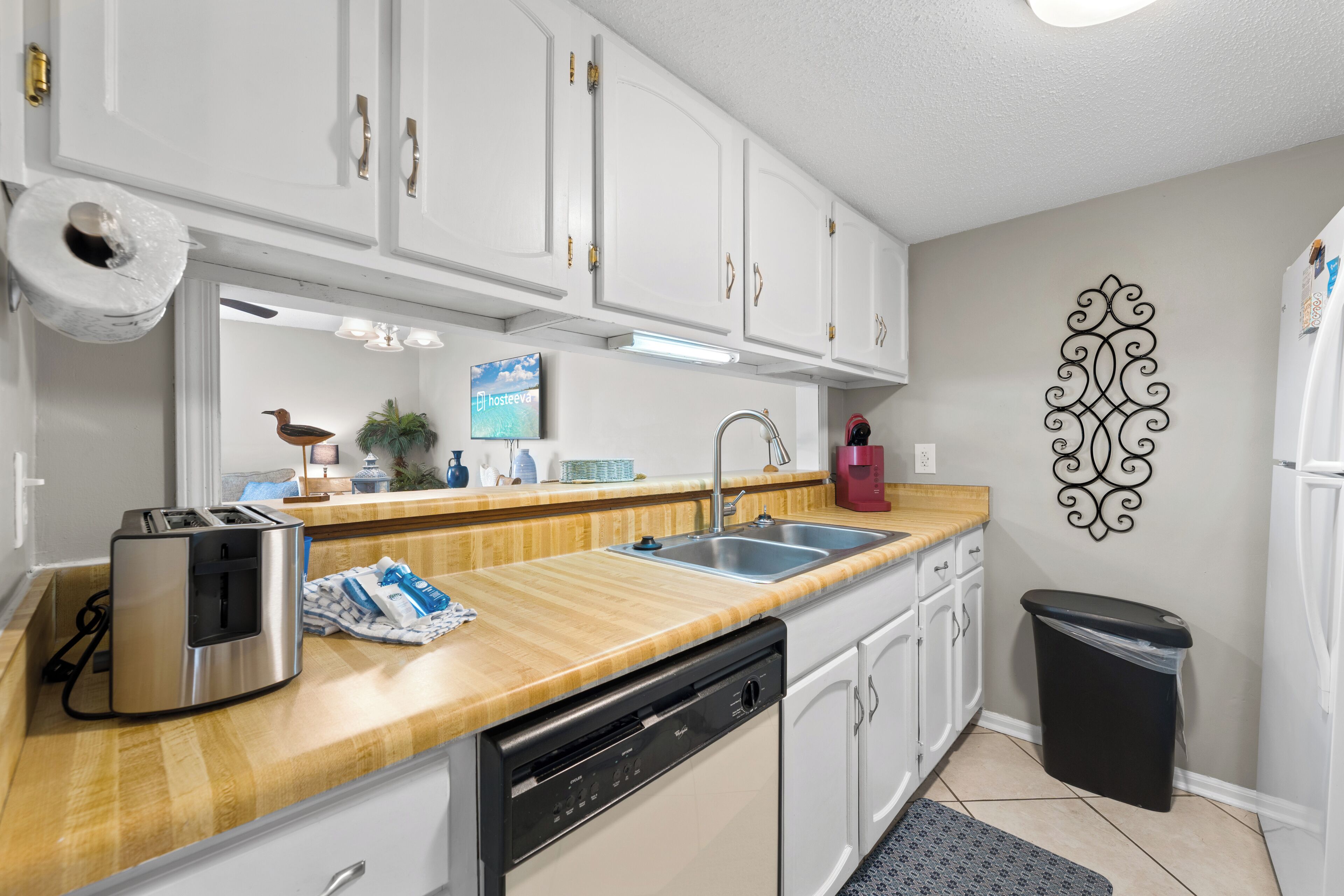 A modern kitchen with white cabinets, a wooden countertop, a dishwasher, a sink, and a trash bin.