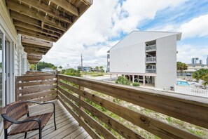 A wooden deck with a chair, overlooking a modern building with a pool. - Gulf View 8 (Gulf Shores)
