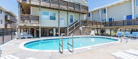 Zona de piscina con terraza de madera, sillas de descanso y un cartel con las normas de la piscina.