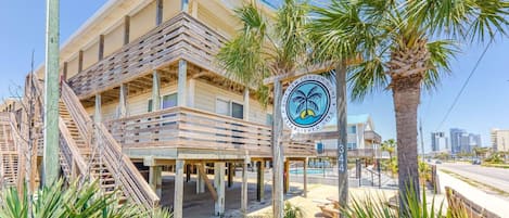 A beachfront property with a wooden deck, palm trees, and a sign indicating Gulf View Condominiums.