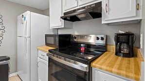 Cocina compacta con refrigerador, microondas, estufa, horno y cafetera.
