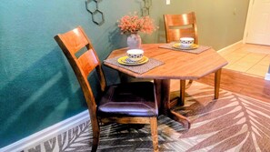 A dining area with a wooden table, two chairs, a vase with flowers, and a patterned rug. - Welcome to the GLO Getaway on Indian Point! A Cozy, Pet Friendly, Condo near SDC (Branson)