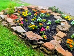 A garden bed with various colorful flowers and plants, surrounded by a stone border.