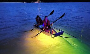 Dos personas en kayak sobre el agua de noche, con iluminación artificial.