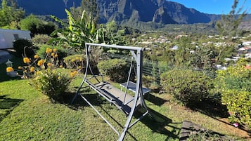 A swing set in a garden with a view of a town and mountains.