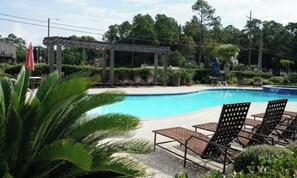 Una piscina con lettini, una zona relax all'ombra e vegetazione circostante.
